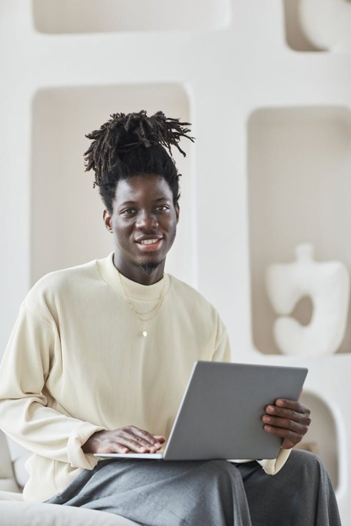 Smiling man with afro hair working on a laptop in a modern indoor setting.